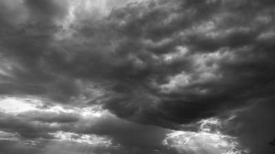 Black and white photo of a sky filled with dark, dramatic clouds, with some light breaking through at the edges.