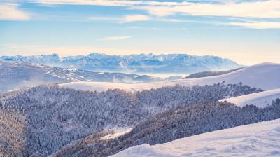 Snow-covered mountains and forested hills under a clear blue sky with distant peaks in the background.