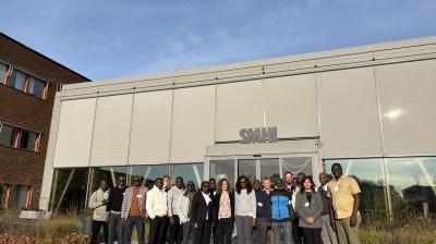A group of people stands in front of a building labeled "SMHI" on a sunny day. The building has large windows and a concrete exterior.