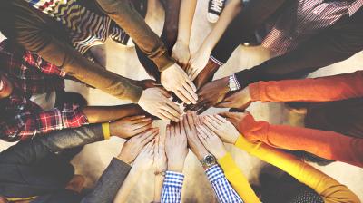 A diverse group of individuals extends their hands into the center of a circle, symbolizing unity and teamwork.