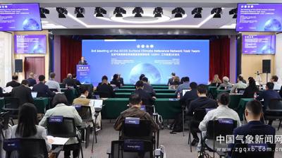 A conference room with attendees viewing a large screen displaying the "3rd Meeting of the GCOS Surface Climate Reference Network Task Team." Chairs and tables are arranged in rows.