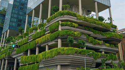 A modern building with tiered green terraces and abundant plants, featuring a blend of glass and concrete architecture.