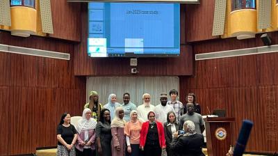 A group of people poses for a photo in front of a large screen displaying "Jan-2023 case study" in a wood-paneled auditorium.