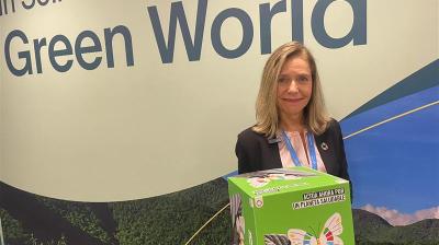 A woman holds a box with a butterfly design in front of a wall with the text "In Solidarity for a Green World.