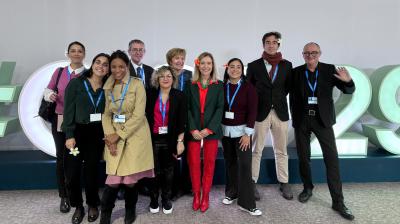 A group of ten people standing in front of large, stylized numbers and letters. Some are smiling, and they all have lanyards around their necks.