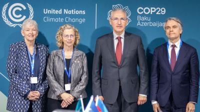Four individuals stand in front of a COP29 Baku Azerbaijan backdrop, featuring United Nations Climate Change logos. They are dressed formally and wearing conference badges.