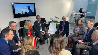 A group of people in business attire sit in a circle having a discussion in a conference room.