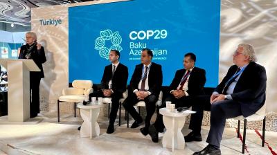 Five people in formal attire sit and stand on a stage with a "COP29 Baku Azerbaijan" backdrop.