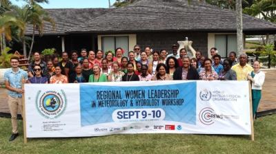 Group photo of attendees at the Regional Women Leadership in Meteorology & Hydrology Workshop, holding a banner with event details and logos, set outdoors with greenery and a building in the background.