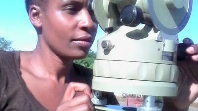 A person using a theodolite outdoors under a clear blue sky.