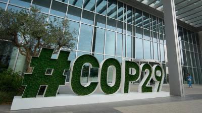 Large green hashtag sign reading "#COP29" outside a modern glass building with trees nearby.