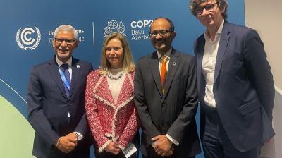 Four people in business attire stand in front of a COP28 banner with the UN logo.