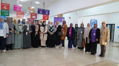 A group of people stands together indoors in front of colorful posters. Some are wearing badges and headscarves.