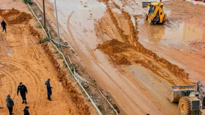 Flooded street with muddy water, people walking, and construction vehicles working near a PetroOil station.