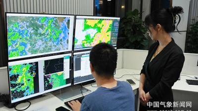 Two people in an office view weather maps and data on multiple monitors in a control room setting.