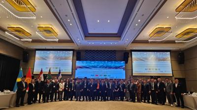 A group of people in formal attire posing in a large conference hall with multiple flags and two large screens in the background.