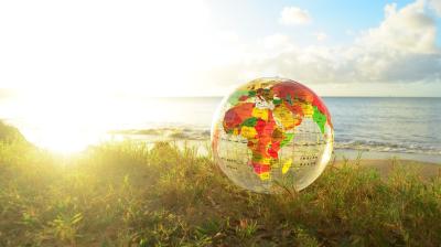 An inflatable globe sits on grass near a beach, with the ocean and sky in the background.