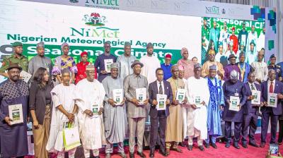 A group of people, mostly men, stand on a stage holding booklets. The banner behind reads "Nigerian Meteorological Agency" with "Seasonal Climate" partially visible.