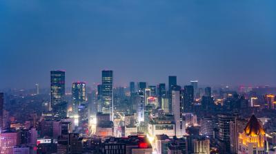 Aerial view of a city skyline at night with illuminated skyscrapers and buildings under a deep blue sky.