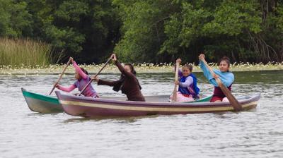 People paddling two canoes on a calm lake surrounded by lush greenery.