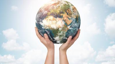 Hands holding up a globe against a cloudy sky background.