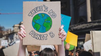 A person holds a sign with a drawing of Earth and the words “There’s No Planet B” at a public protest or demonstration.