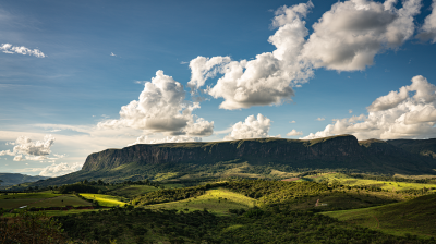 A wide plateau rises above a green, sunlit valley under a blue sky with scattered white clouds.