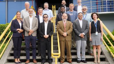 A group of fourteen people poses for a photo on outdoor stairs in front of a building, dressed in business and casual attire.