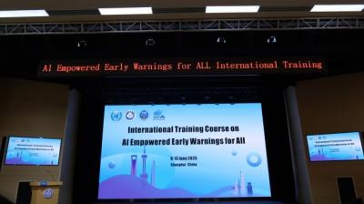 A conference stage displays a banner and digital sign for the "International Training Course on AI Empowered Early Warnings for All," held in Shanghai, China, June 2025.