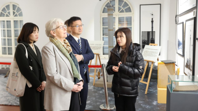 Four people stand together in a museum or gallery, listening to a guide explain framed photographs on the wall.