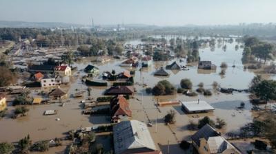 Aerial view of a residential area heavily flooded, with houses partially submerged and trees surrounded by water.