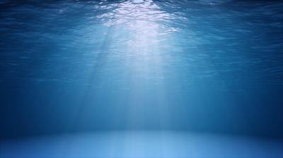 Sunlight filters through clear blue ocean water, casting rays onto the calm, sandy seafloor below.