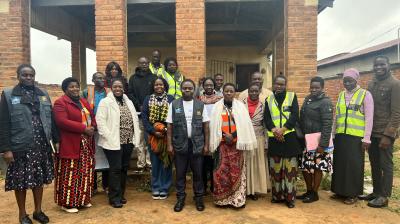 A group of adults stand together outside a brick building, some wearing reflective vests and others in patterned clothing, posing for a group photo.