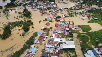 Aerial view of a flooded town with numerous buildings partially submerged in muddy water and surrounding areas also impacted by the flood.