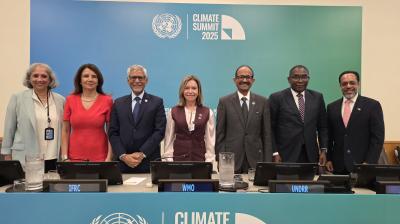 Seven delegates stand behind a table at the Climate Summit 2025, with UN and organization logos displayed on the wall and table in a conference room setting.