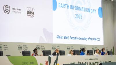 Panelists sit on stage at the COP30 Belém Climate Summit, with a large screen displaying "Earth Information Day 2025" and the name Simon Stiell, Executive Secretary of the UNFCCC.