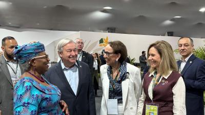 A group of five people, including two women in business attire and one in a blue patterned outfit, stand together indoors, conversing and smiling at an event.