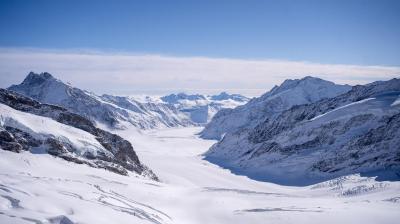 Snow-covered mountains and a glacier under a clear blue sky, with rugged peaks and a wide valley extending into the distance.