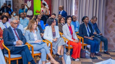 A group of people in business attire are seated in rows at an indoor conference or meeting, listening attentively to a presentation.