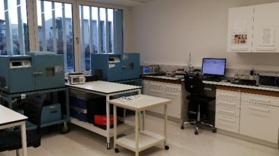 Laboratory room with blue scientific equipment, workstations, computers, white cabinets, and large windows letting in natural light.