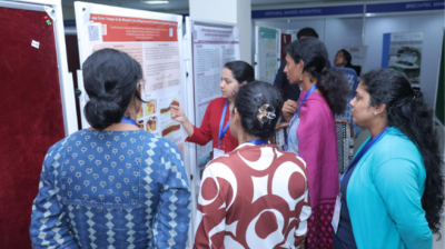 A group of women stand around a presenter explaining information displayed on a scientific poster at an indoor event or conference.