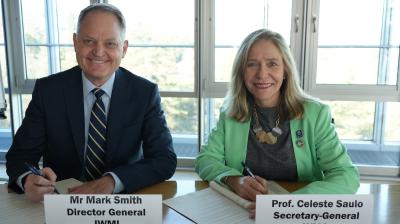 Two people sit at a table, each holding a pen and papers, with nameplates reading "Mr Mark Smith Director General IWMI" and "Prof. Celeste Saulo Secretary-General WMO.