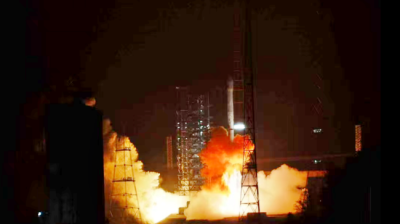 A rocket launches at night, emitting bright flames and smoke, with metal structures and a lit-up tower visible in the background. Chinese text is present in the bottom right corner.