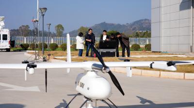 Four people stand by a black equipment case outdoors while a large white drone marked “XAMY” rests on the pavement in the foreground.