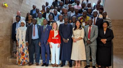 A large group of people, dressed in formal and traditional attire, pose for a group photo on a staircase in an indoor setting.