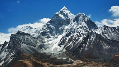 Snow-capped mountain peaks rise under a clear blue sky, with rocky slopes and patches of brown terrain in the foreground.