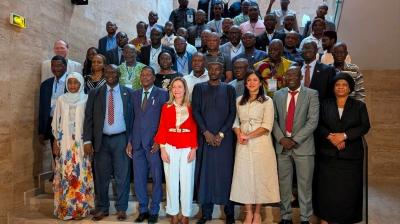A large group of men and women in formal attire stand on stairs posing for a group photo indoors.