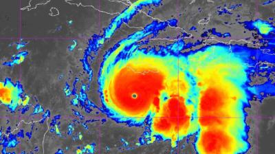 Satellite image shows a large hurricane with a clear eye, displaying intense red and yellow cloud bands indicating strong storm activity approaching land.