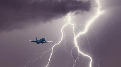 A commercial airplane flies near a large lightning strike in a dark, cloudy sky.