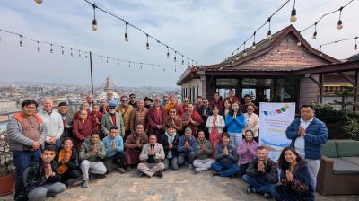A group of people pose for a photo on a rooftop with string lights, a city view, and a banner that reads "HIA Daily." Most of them have their palms together in a greeting gesture.